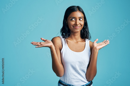 Options, thinking and woman with a gesture in a studio with a confused, unsure or uncertain face. Decision, doubt and Indian female model with choice or shrug hand sign by blue background with mockup photo