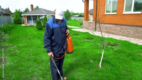 A man works in the garden, spraying weeds from a sprayer