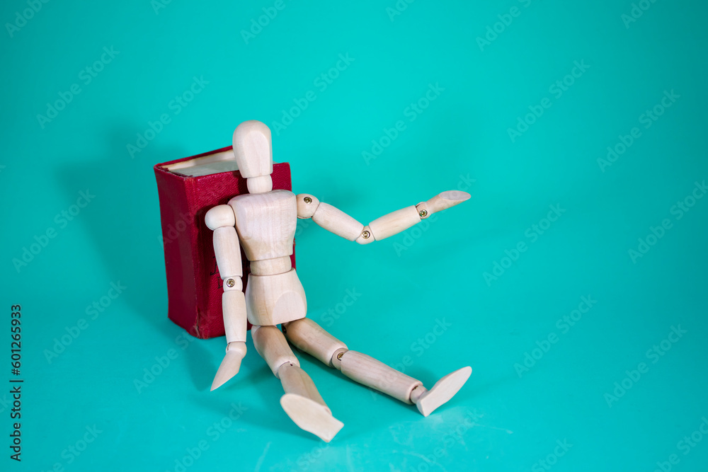 Wood Man and Book. Wooden Figure Sitting. Cheerful Wooden Doll on a Blue Background with a Book. Reading Books Shows Learning. Education concept. Wood Man and Book. Wooden Figure Sitting. Cheerful Wooden Doll on a Blue Background with a Book. Reading Books Shows Learning. Education concept.