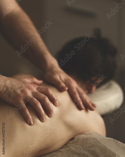 Woman is getting massage. Back massage. Dark-haired woman lies face down on couch. Masseur's hands on back. Relax, spa, body care. Side view. Soft focus.