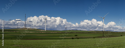 Windmills in the mountains. Mountain range with green grass, white fluffy clouds on the blue sky.