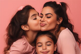 Hispanic mother and children kissing and hugging on a pink background