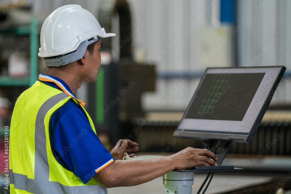 A worker is using a computer to control a steel laser cutting machine in a factory. A worker is using a computer to control a steel laser cutting machine in a factory.