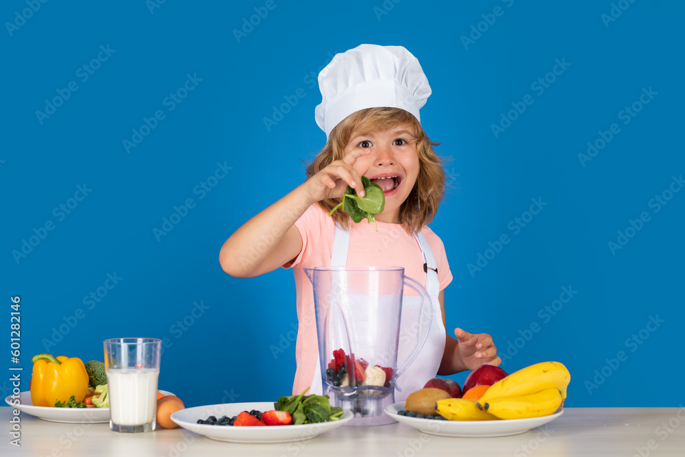 Excited funny chef cook. Kid boy in chef hat and apron hold spinach cooking preparing meal. Little cook with vegetables at kitchen. Natural kids food. Excited funny chef cook. Kid boy in chef hat and apron hold spinach cooking preparing meal. Little cook with vegetables at kitchen. Natural kids food.