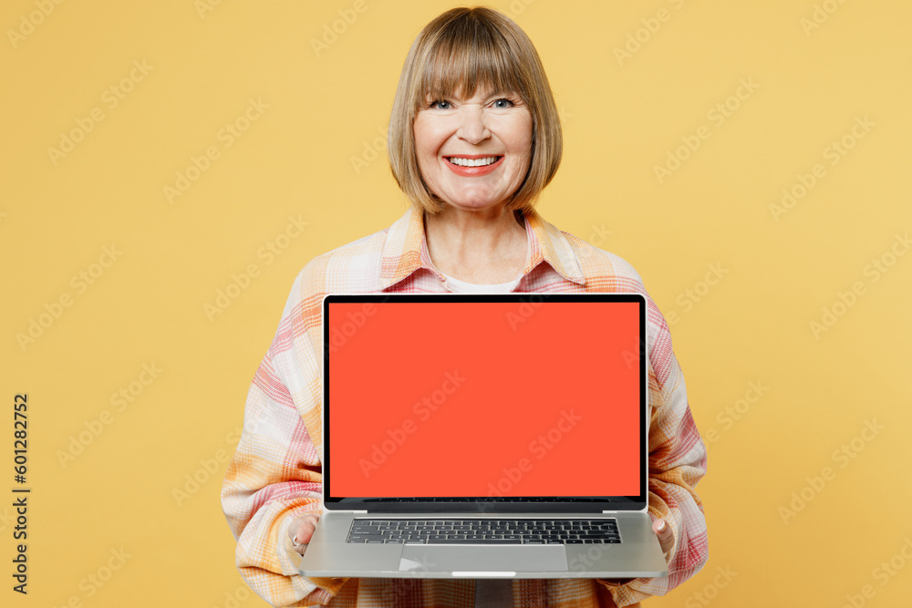 Elderly happy fun smart blonde IT woman 50s years old she wear casual clothes hold use work on laptop pc computer with blank screen workspace area isolated on plain yellow background studio portrait.