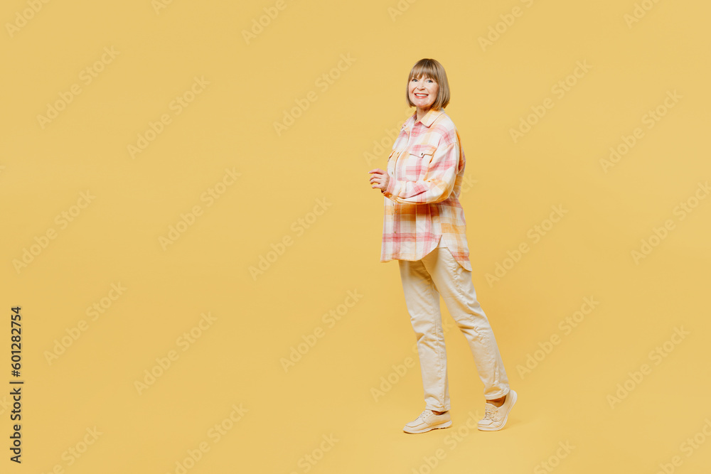 Full body side view elderly smiling happy blonde woman 50s years old wear casual clothes walking going looking camera strolling isolated on plain yellow background studio portrait. Lifestyle concept.