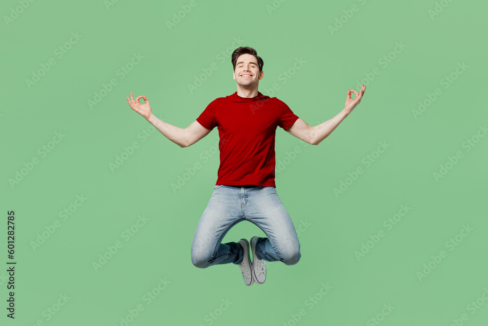 Full body young spiritual man he wears red t-shirt casual clothes jump high hold spreading hands in yoga om aum gesture relax meditate try to calm down isolated on plain pastel light green background. Full body young spiritual man he wears red t-shirt casual clothes jump high hold spreading hands in yoga om aum gesture relax meditate try to calm down isolated on plain pastel light green background.