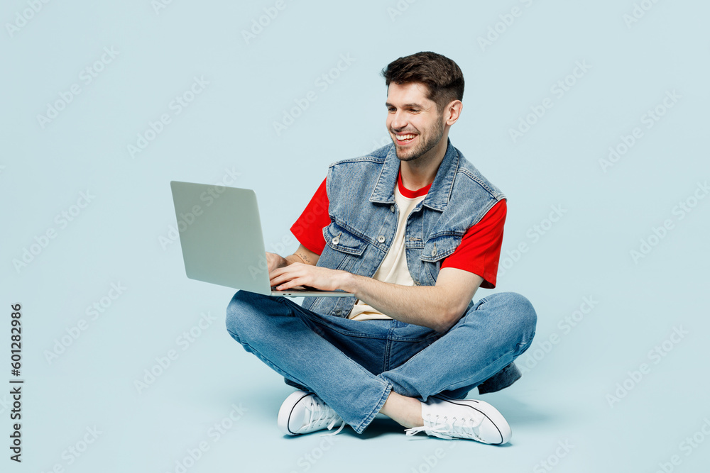 Full body smiling fun young happy IT man wears denim vest red t-shirt casual clothes sit hold use work on laptop pc computer chatting online isolated on plain pastel light blue cyan background studio. - obrazy, fototapety, plakaty 