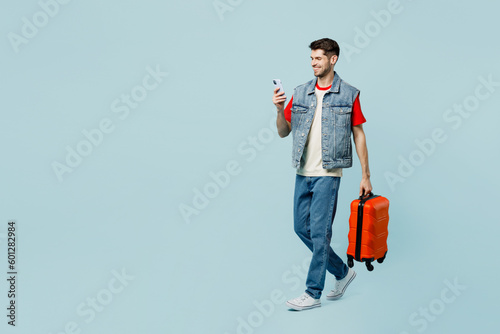 Traveler man in casual clothes hold suitcase use mobile cell phone isolated on plain pastel blue cyan background Tourist travel abroad in free spare time rest getaway Air flight trip journey concept #601282984