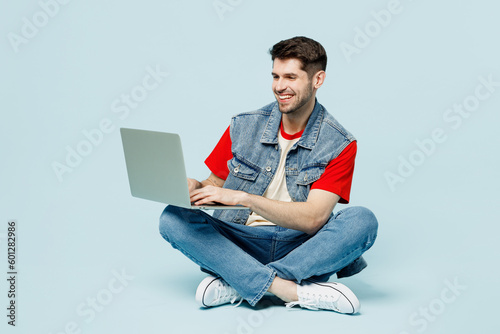 Fotobehang Full body smiling fun young happy IT man wears denim vest red t-shirt casual clothes sit hold use work on laptop pc computer chatting online isolated on plain pastel light blue cyan background studio