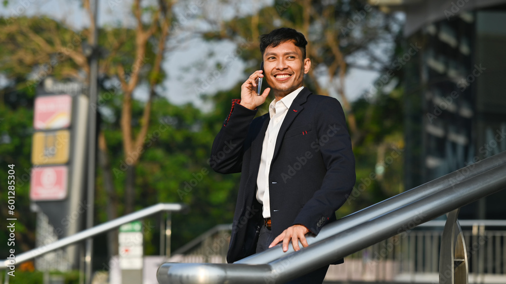 Handsome businessman talking on mobile phone while standing outdoor with cityscape background in early morning Handsome businessman talking on mobile phone while standing outdoor with cityscape background in early morning