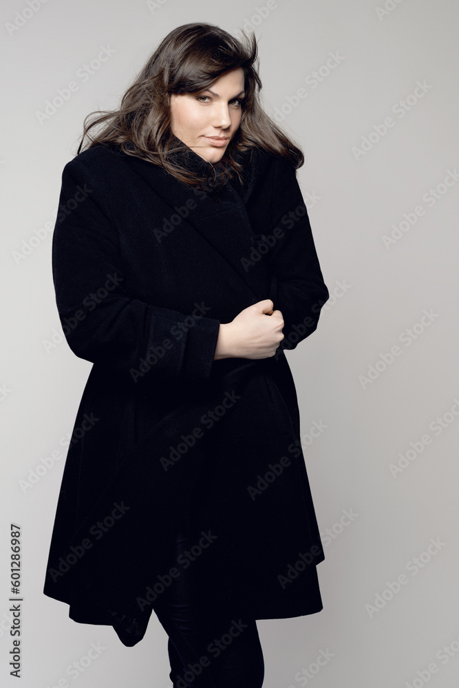 Fototapeta premium Woman, fashion and portrait of plus size model posing in winter clothing against a grey studio background. Isolated female person standing with stylish black coat, body or warm fashionable clothes