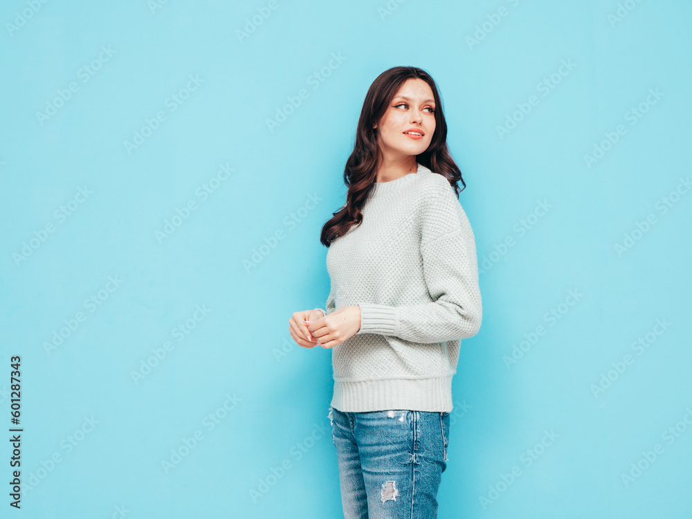 Young beautiful smiling female in trendy summer jeans and warm winter sweater clothes. Sexy carefree woman posing near blue wall in studio. Positive model. Cheerful and happy. Isolated Young beautiful smiling female in trendy summer jeans and warm winter sweater clothes. Sexy carefree woman posing near blue wall in studio. Positive model. Cheerful and happy. Isolated