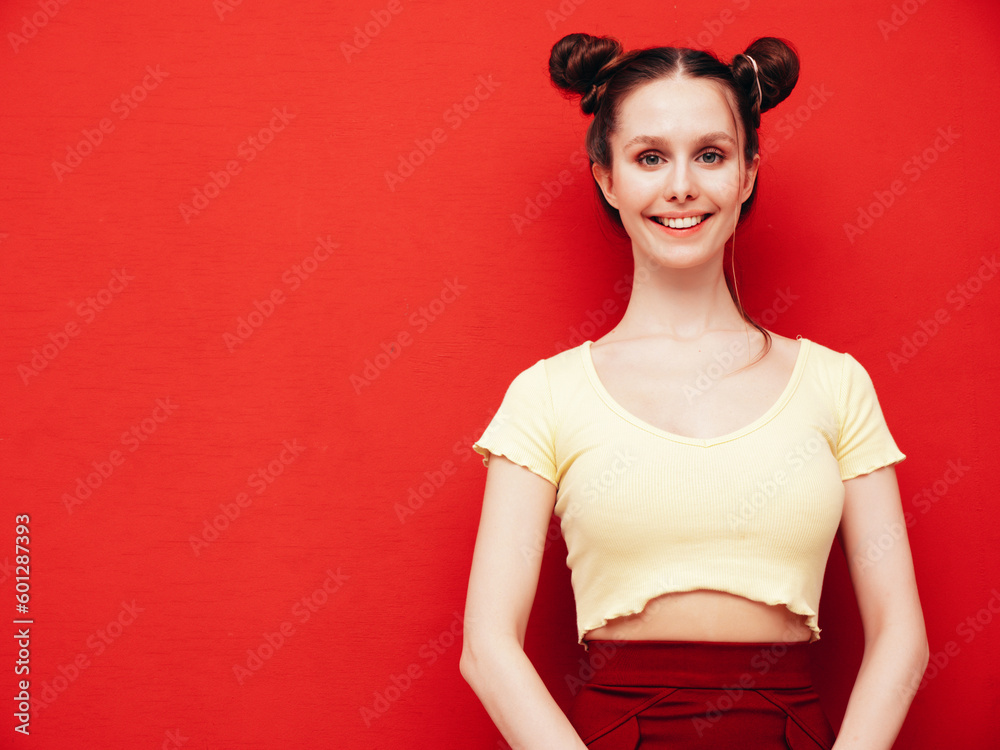 Young beautiful smiling female in trendy summer yellow t-shirt and skirt. Carefree woman with two horns hairstyle posing near red wall in studio. Positive model having fun. Cheerful and happy Young beautiful smiling female in trendy summer yellow t-shirt and skirt. Carefree woman with two horns hairstyle posing near red wall in studio. Positive model having fun. Cheerful and happy