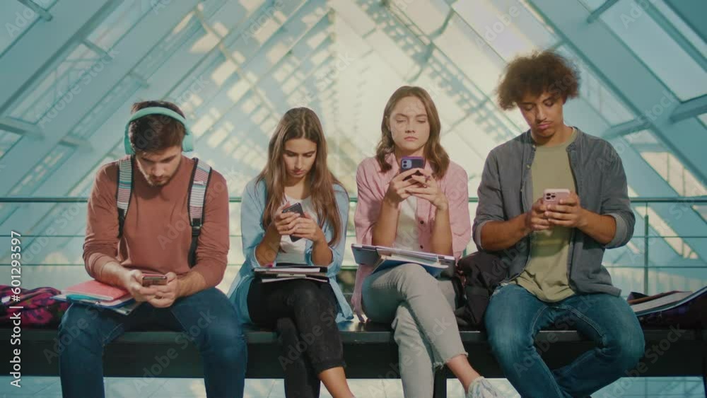 Group of Students Using Smartphones - Students Sitting on a Bench and Typing on their Smartphones. Break. Concept of Digital Education, Future Technologies, Robotization of Learning, Global Education Group of Students Using Smartphones - Students Sitting on a Bench and Typing on their Smartphones. Break. Concept of Digital Education, Future Technologies, Robotization of Learning, Global Education