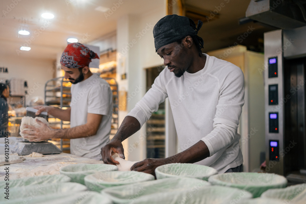 Black baker kneading in bakery with colleague Black baker kneading in bakery with colleague