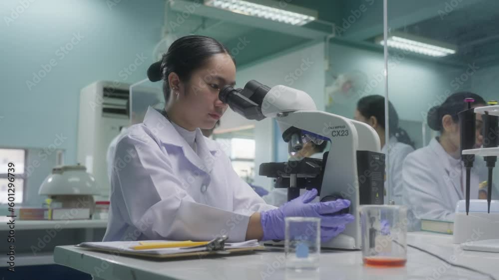 Medical Technology Student Using A Microscope With Professor In The Background Inside The Laboratory. - close up Medical Technology Student Using A Microscope With Professor In The Background Inside The Laboratory. - close up