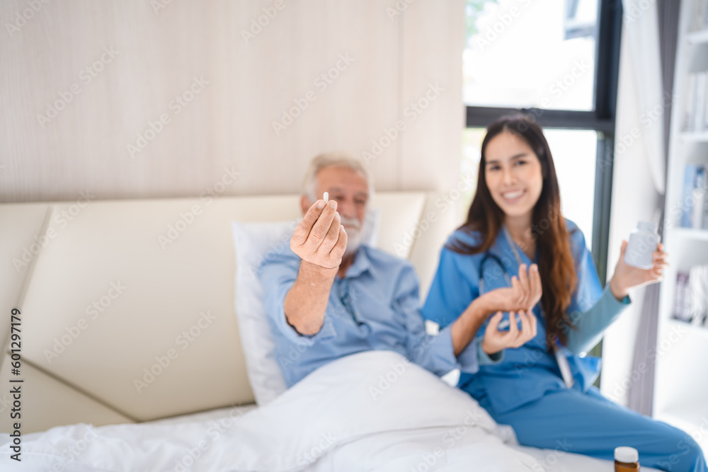 Smiling young nurse in hospital and health care center giving routine medications to happy and cheerful senior patient lying and sitting on bed while having a fun conversation Smiling young nurse in hospital and health care center giving routine medications to happy and cheerful senior patient lying and sitting on bed while having a fun conversation