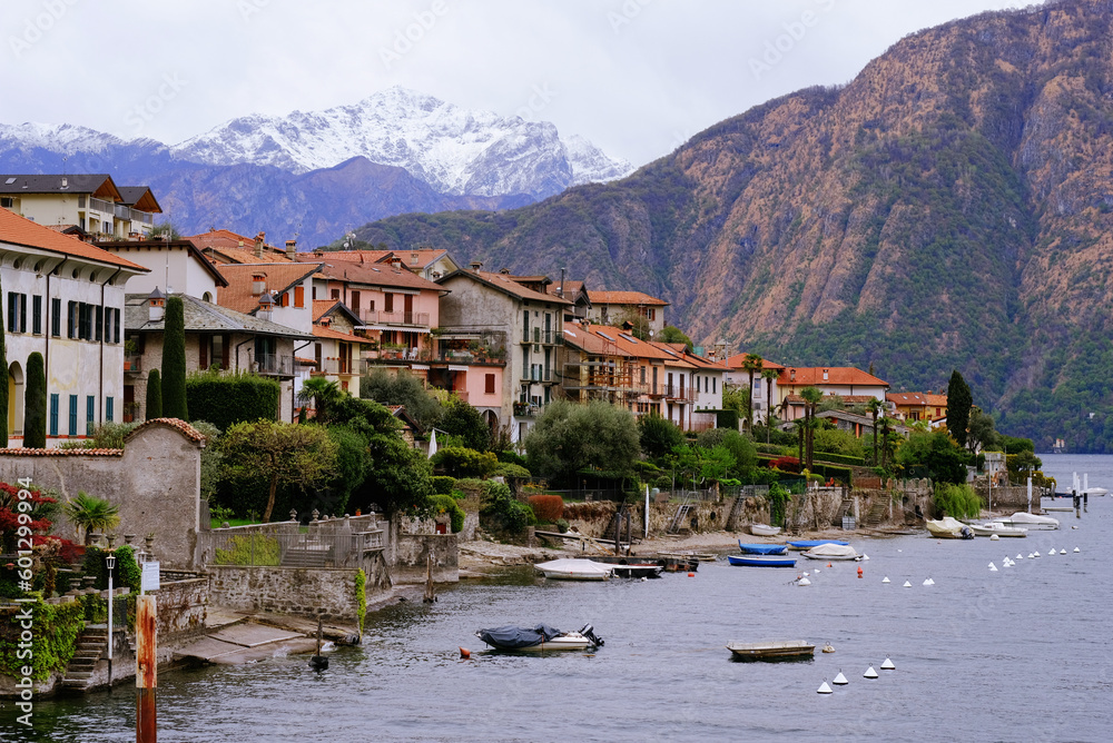 Como, Italy - 04 20 2023: Houses with red tile roofs on the cliffs and surrounded by mountains, alpine peaks and a beautiful lake.
