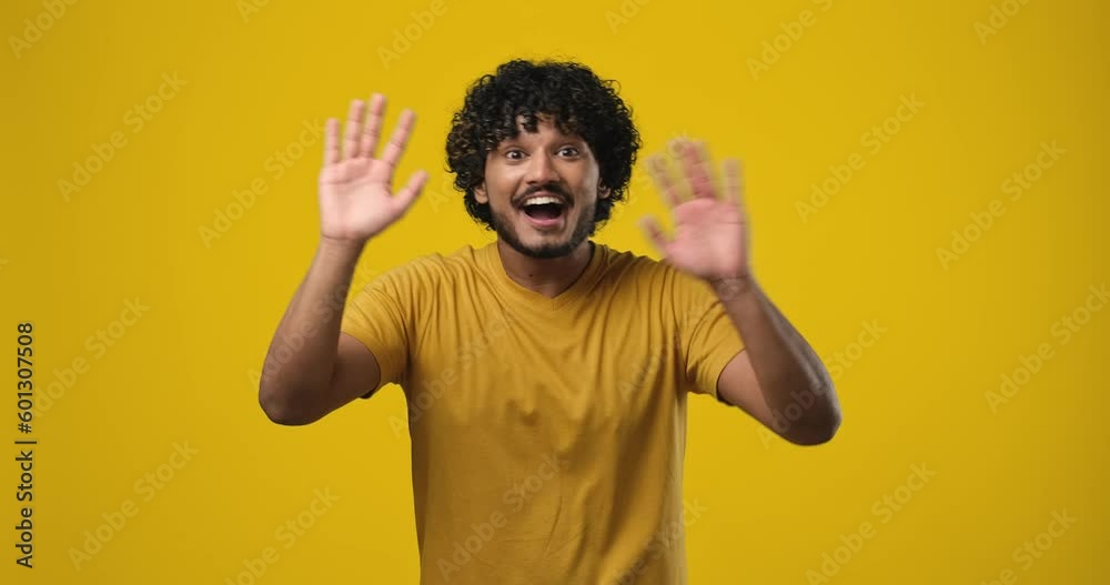 Young indian man waves hand palm in hello gesture welcomes someone expresses positive emotion standing over orange studio background Young indian man waves hand palm in hello gesture welcomes someone expresses positive emotion standing over orange studio background
