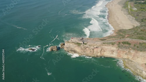 rocky cliff of nazare beach with crashing waves of the atlantic ocean breaking against the shore below photo