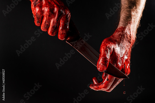 A man wipes a bloody knife with his hand on a black background. 