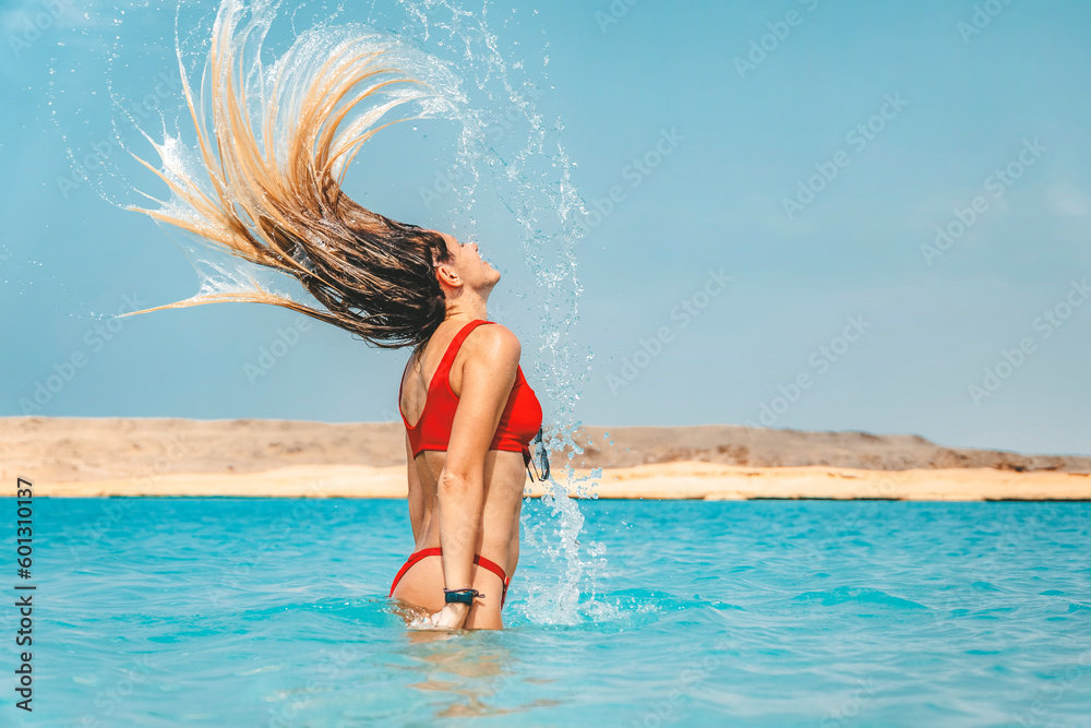 Naklejka premium Woman splashing water with her hair in ocean. Selective focus. Hair in motion blur.