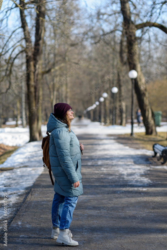 Smiling young woman in blue parka walking at park at sunny spring day. Smiling young woman in blue parka walking at park at sunny spring day.