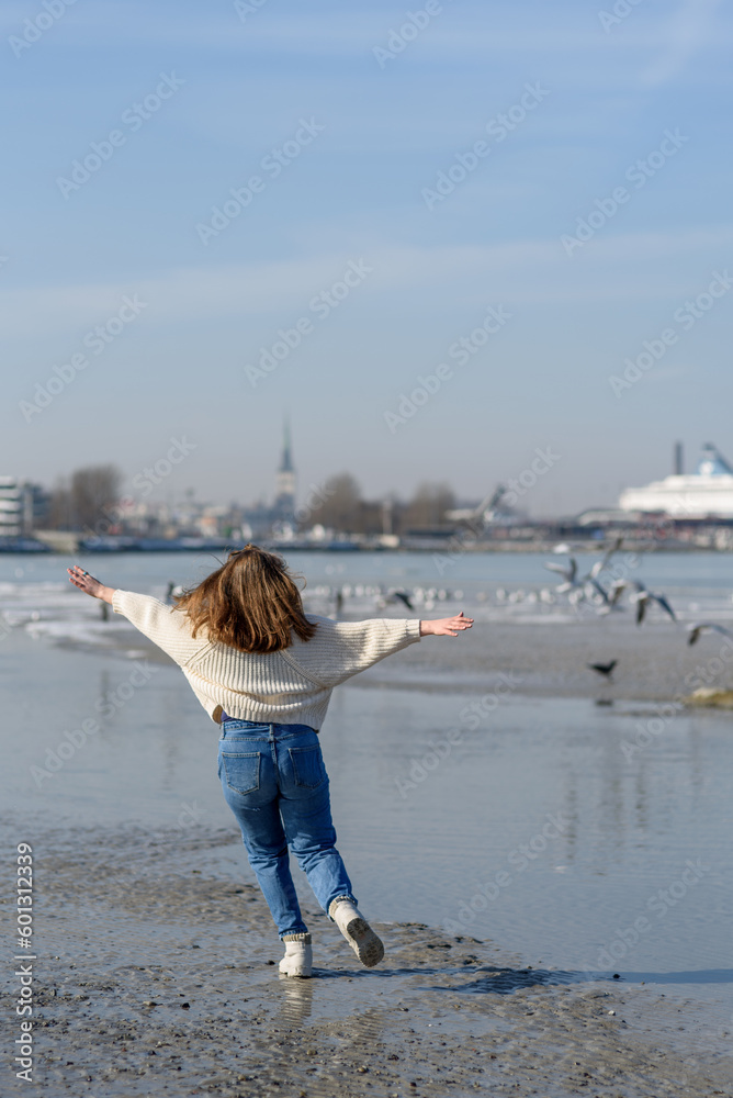 Smiling young woman in knitted sweater running at beach