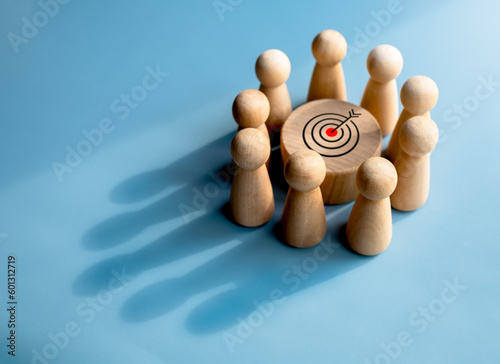 Target icon on round wood block surrounded with small wooden human figures made a crown shadow shape on blue background. Business goal and success, leadership, teamwork power and confidence concepts. photo