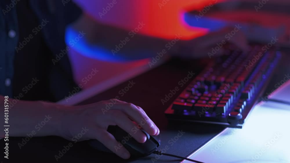 Nervous gamer. Night entertainment. Twitchy man hands typing on keypad fast and using mouse playing online video game in dark room with neon illumination. Nervous gamer. Night entertainment. Twitchy man hands typing on keypad fast and using mouse playing online video game in dark room with neon illumination.