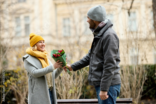 Mid adult couple relaxing in the park with man offering bouquet of flowers