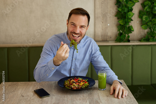 Mid adult man enjoys eating salad and drinking smoothie in salad bar
