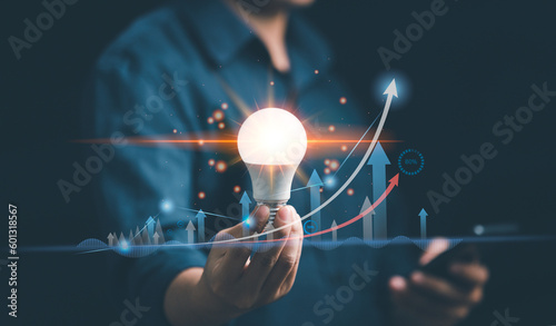 Man hand holding bright light bulb with graph economic
