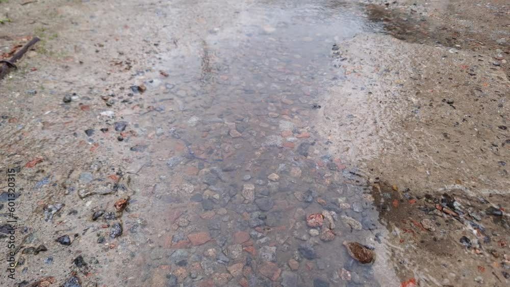 Puddle of rainwater on concrete and gravel surface during rain