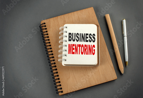 BUSINESS MENTORING text on notebook with pen and pencil on grey background