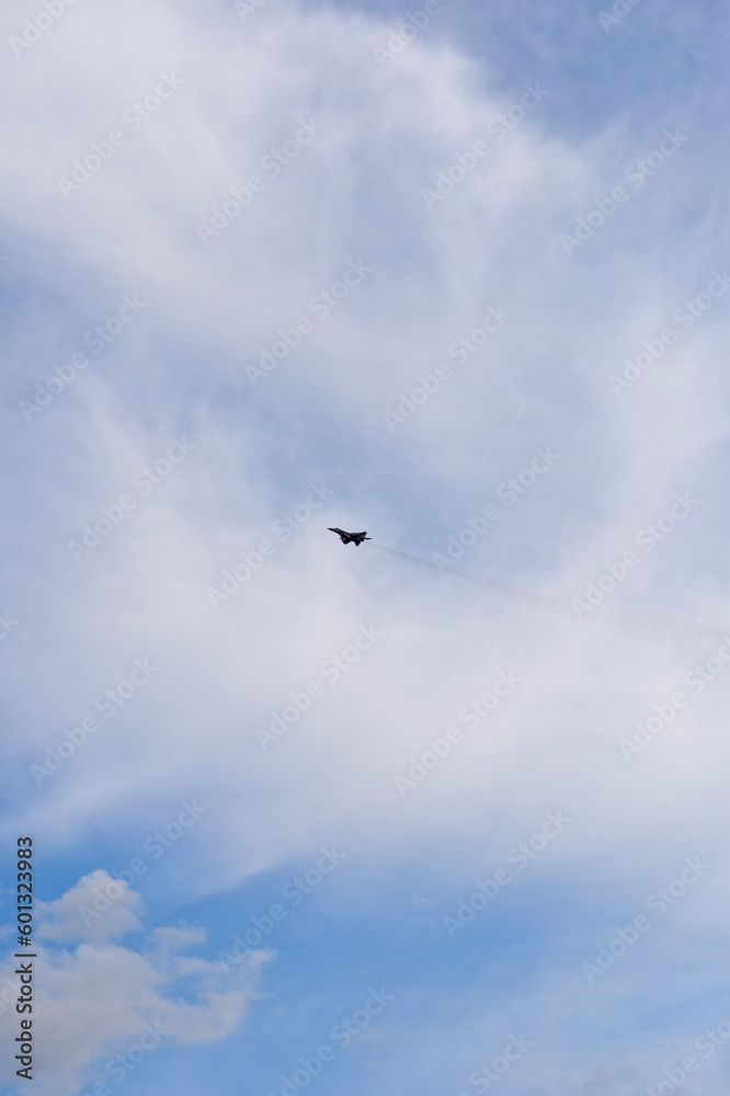 A military aircraft flying high in the sky against a blue sky and clouds.