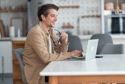A smiling male freelancer working over the laptop and sitting at the dining table.