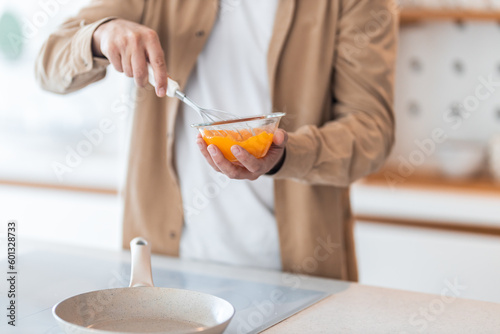 Fotografija Close-up of a man's hands, holding a bowl with beaten eggs and making an omelet