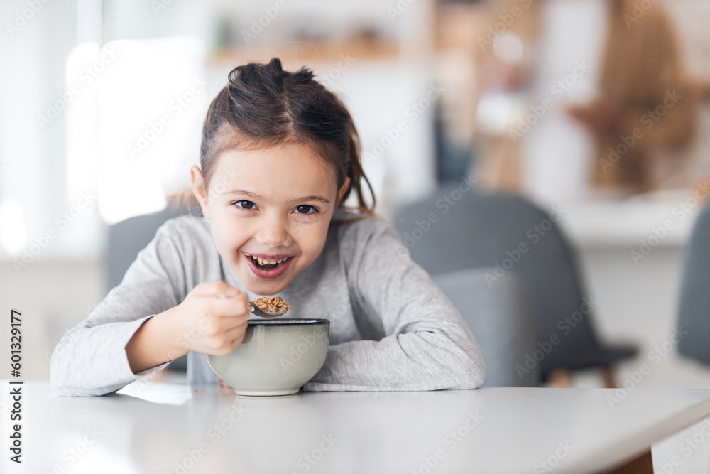 Portrait of a sweet little girl sitting at the dining table and eating her healthy breakfast.