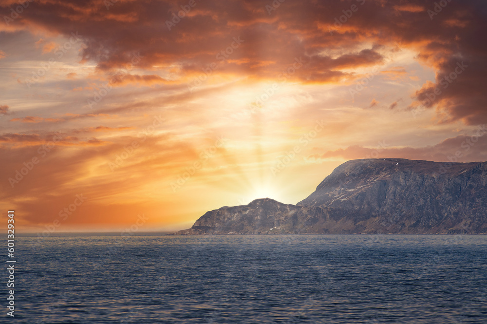 View from the sea to the West Cape in Norway at sunset. Sun shines over the rocks