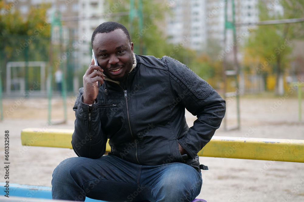 Obraz premium African american man sits at sport ground and speaks on smartphone