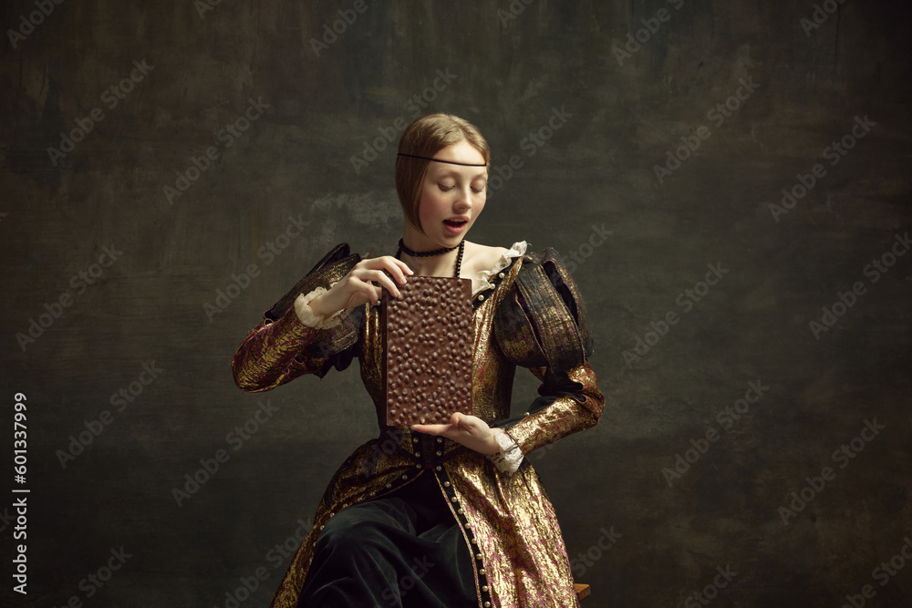 Fototapeta premium Portrait of young girl, medieval royal person, pretty princess in vintage dress holding giant chocolate bar over dark green background. Concept of history, renaissance art remake, comparison of eras
