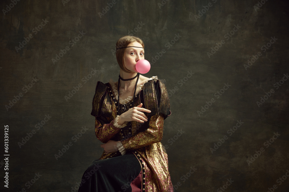 Portrait of pretty young girl, medieval princess in vintage dress posing with bubble gum against dark green background. Concept of history, renaissance art remake, comparison of eras, modernity - obrazy, fototapety, plakaty 