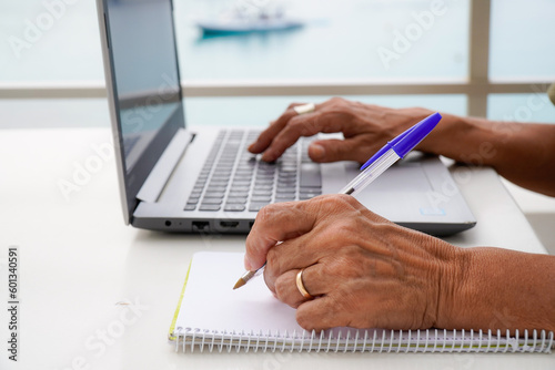 left handed unrecognizable woman works with the computer and writes in the notebook outside. international left handers day