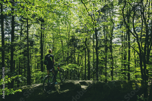 Man standing on rock with MTB bike in lush green forest