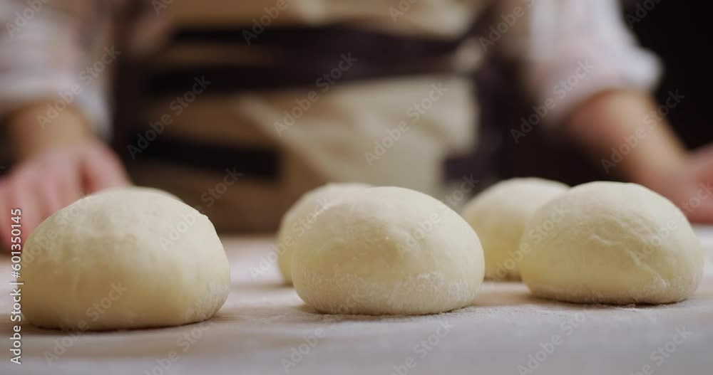 The baker rolls out the dough for buns on the board. Working in a bakery. 4k video The baker rolls out the dough for buns on the board. Working in a bakery. 4k video