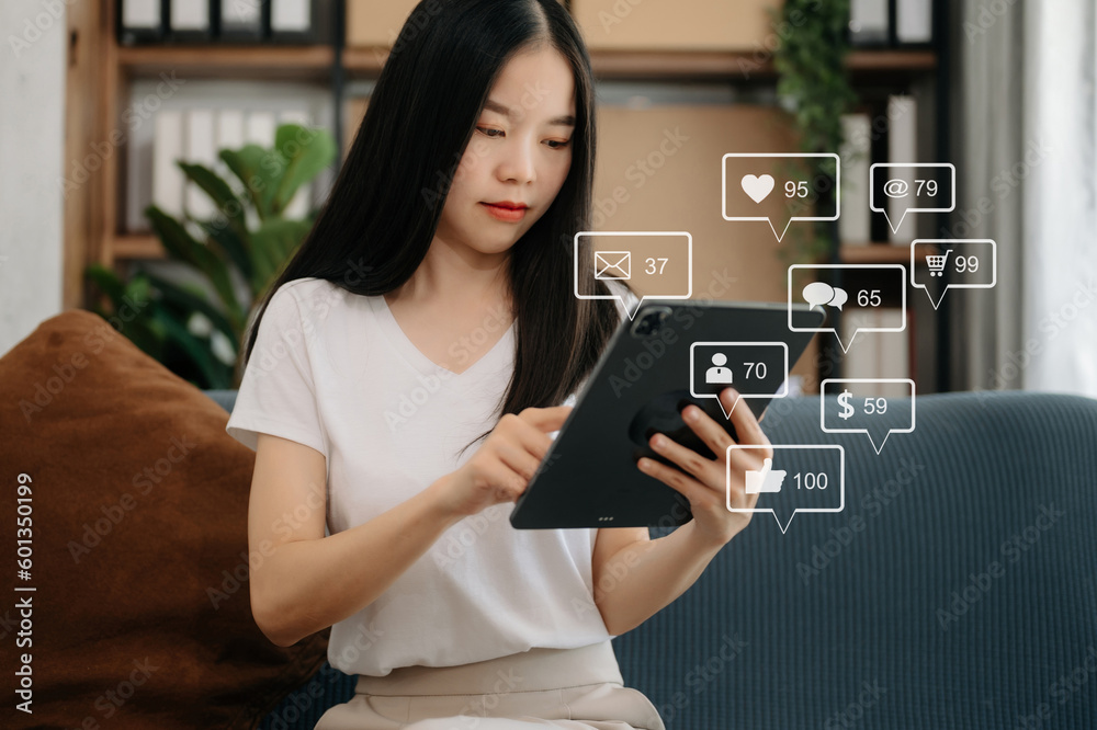 Asian woman typing smartphone, keyboard with laptop computer of Social media and Marketing virtual icons screen concept. on sofa. Asian woman typing smartphone, keyboard with laptop computer of Social media and Marketing virtual icons screen concept. on sofa.