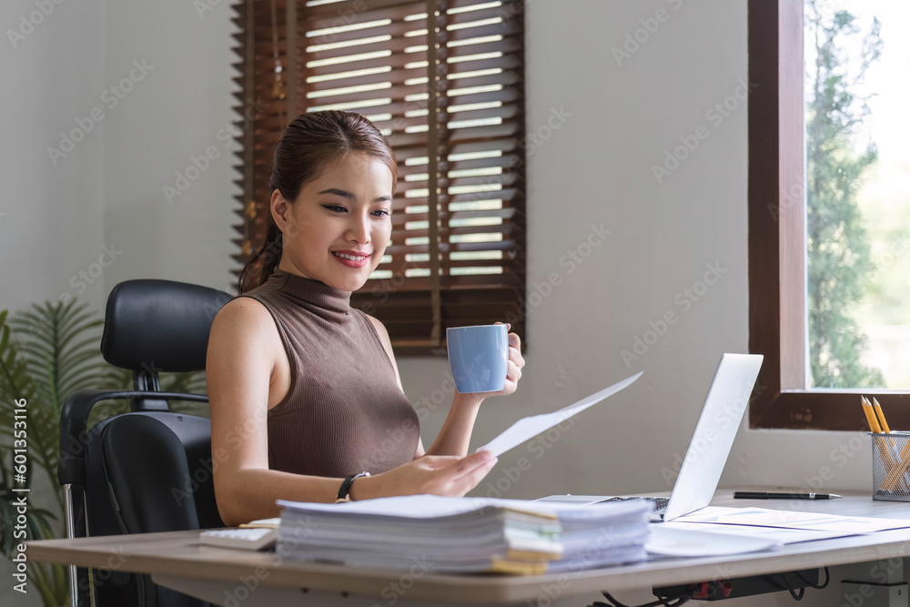 Obraz premium Happy Asian businesswoman working and checking work with laptop computer while having a comfortable cup of coffee at office.