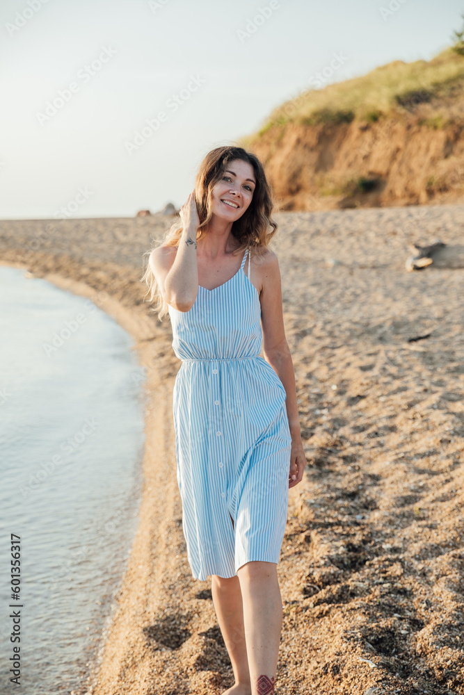 a woman in a sundress walks along the seashore on the beach walk a woman in a sundress walks along the seashore on the beach walk